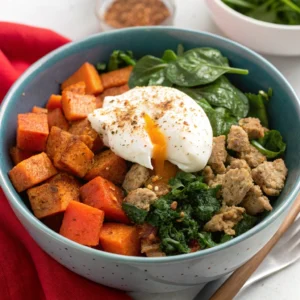 A colorful breakfast bowl with chicken breakfast sausage, roasted sweet potatoes, spinach, and a poached egg.