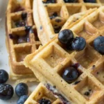 Crispy golden waffles with blueberries baked into the batter, topped with powdered sugar and maple syrup.